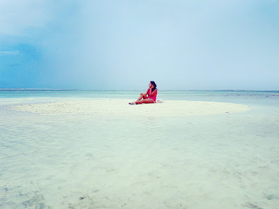 girl sitting in the middle of a tiny sandbank made by low tide