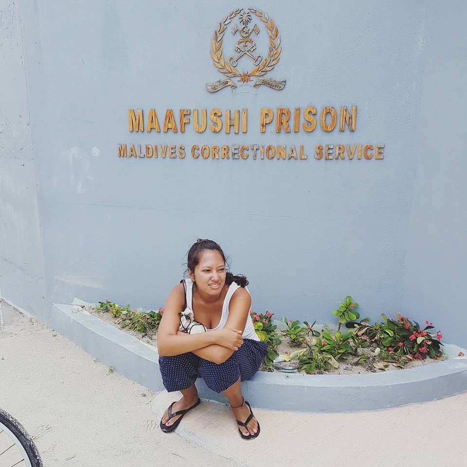girl sitting in front of maafushi prison, looking distressed